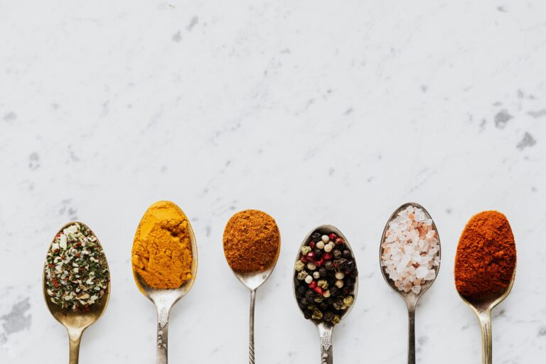 Top view of assorted aromatic condiments arranged together in metal spoons on marble surface used for delicious gourmet meal cooking