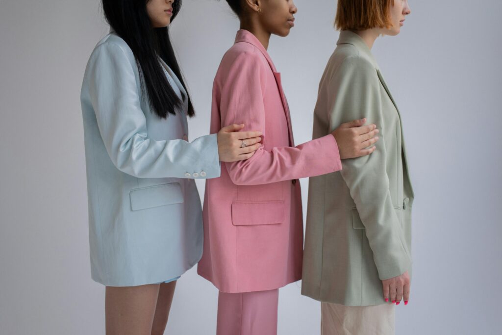 Side view of crop multiracial female models wearing trendy formal outfits standing in row against gray background